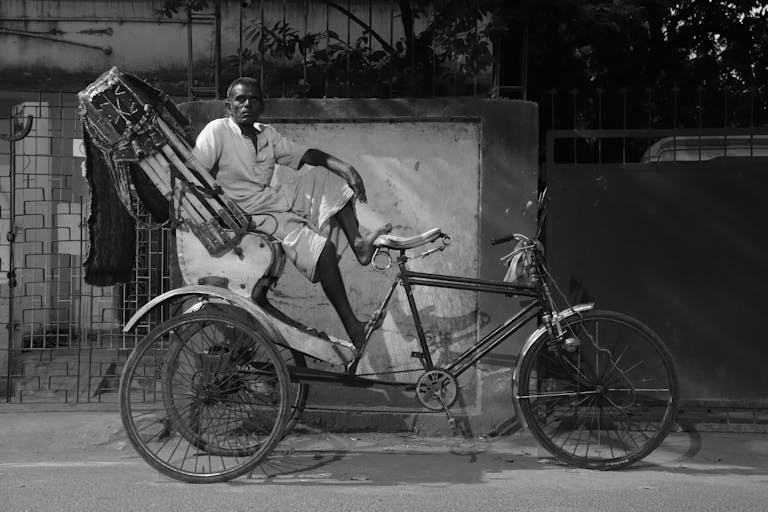 Black and white image of a rickshaw driver resting in Patna's urban environment.